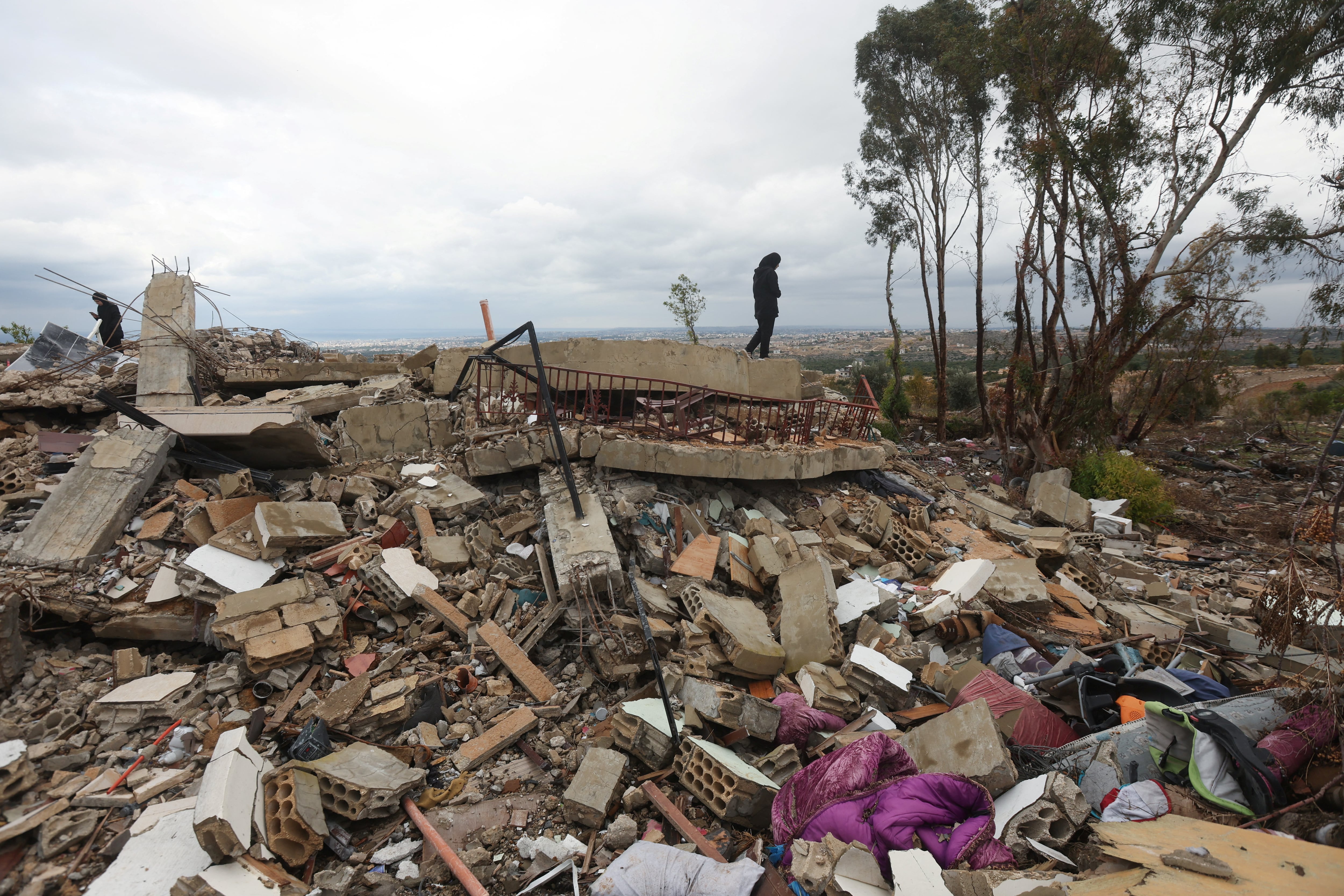 Displaced Lebanese Assaad Bzih's daughter and wife, Zeinab and Asya, walk on rubble near their destroyed home, after a ceasefire between Israel and Hezbollah took effect, in Zibqin southern Lebanon, November 27, 2024. REUTERS/Aziz Taher