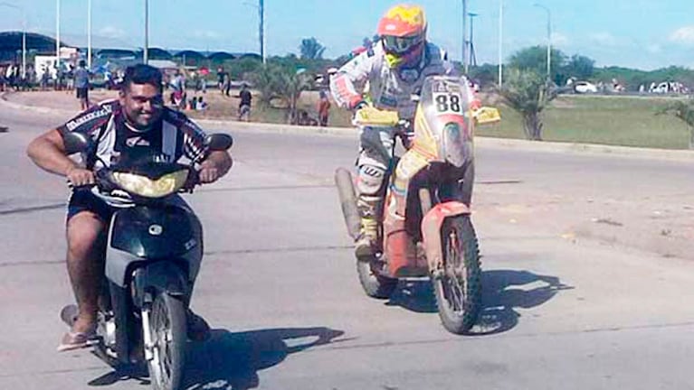 El joven corre con su moto, ante la incrédula mirada del corredor del Dakar.