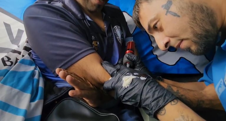 El tatuador haciendo el diseño en la piel del hincha.
