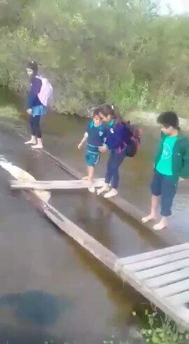 Niños hacen equilibrio sobre un río para llegar a clases