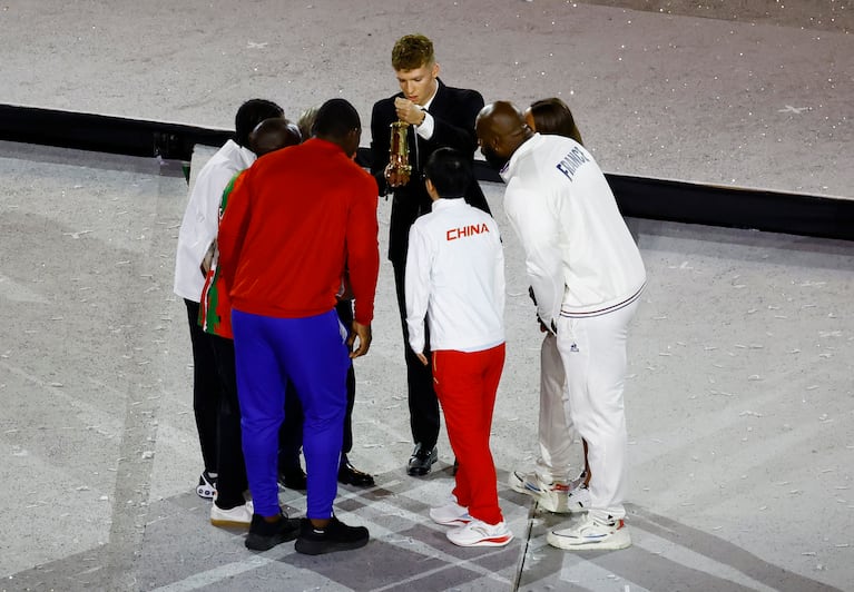 Paris 2024 Olympics - Ceremonies - Paris 2024 Closing Ceremony - Stade de France, Saint-Denis, France - August 11, 2024. French swimmer Leon Marchand holds the Olympic flame lantern as President of International Olympic Committee (IOC) Thomas Bach, with athletes Teddy Riner of France, Mijain Lopez Nunez of Cuba, Yingsha Sun of China, Djankeu Ngamba of Refugee Olympic Team, Eliud Kipchoge of Kenya and Emma McKeon of Australia extinguish the flame. REUTERS/Sarah Meyssonnier