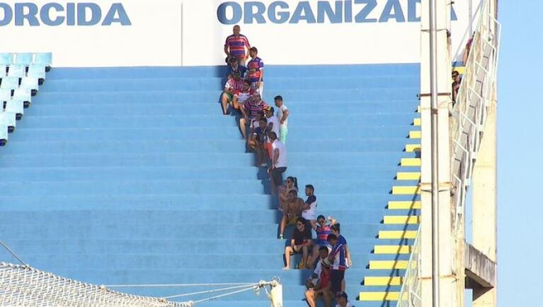 Una hinchada, en fila india a la sombra de un poste