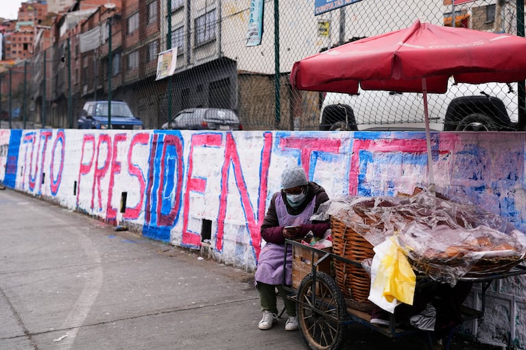 Una mujer vende pan junto a un mural que promueve al candidato presidencial Jorge "Tuto" Quiroga antes de la segunda vuelta electoral, en La Paz, Bolivia, el lunes 13 de octubre de 2025. (AP Foto/Juan Karita)