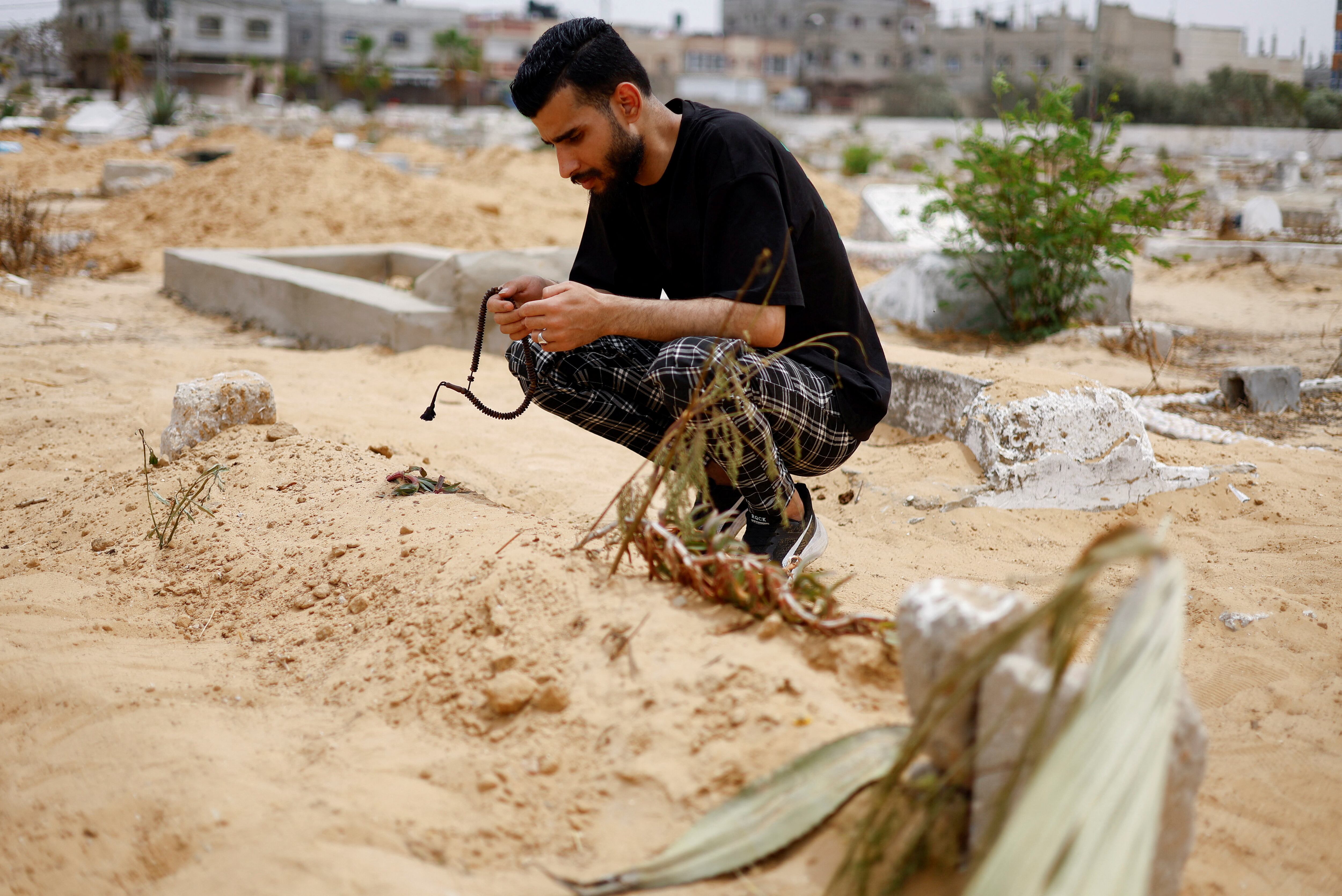 Uncle of Sabreen al-Rouh, a Palestinian baby girl, who died a few days after she was saved from the womb of her dying mother Sabreen al-Sheikh (al-Sakani), killed in an Israeli strike along with her husband Shokri and her daughter Malak, amid the ongoing conflict between Israel and Hamas, crouches next to her grave in Rafah in the southern Gaza Strip, April 26, 2024. REUTERS/Mohammed Salem