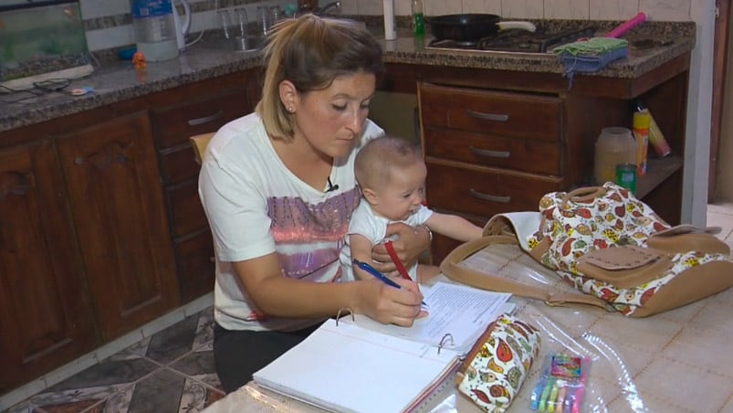 Verónica haciendo las tareas escolares con su bebé en brazos.