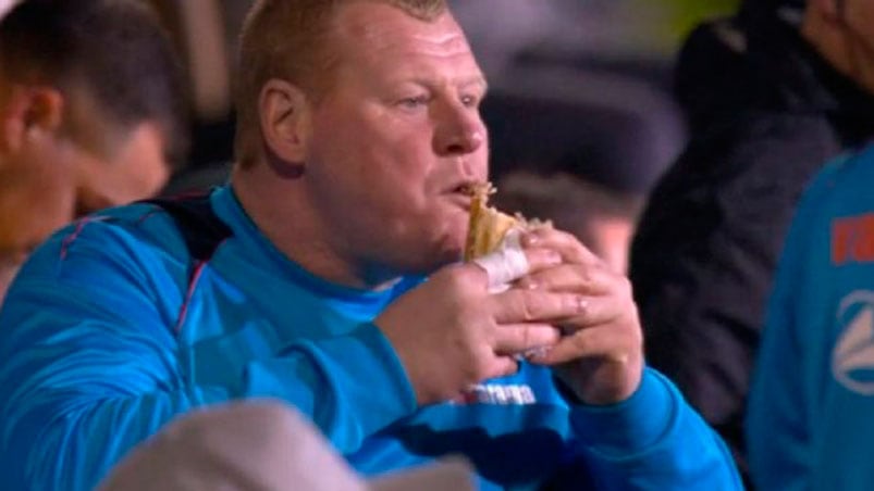 Wayne Shaw le da un mordisco al sándwich en el banco de suplentes.